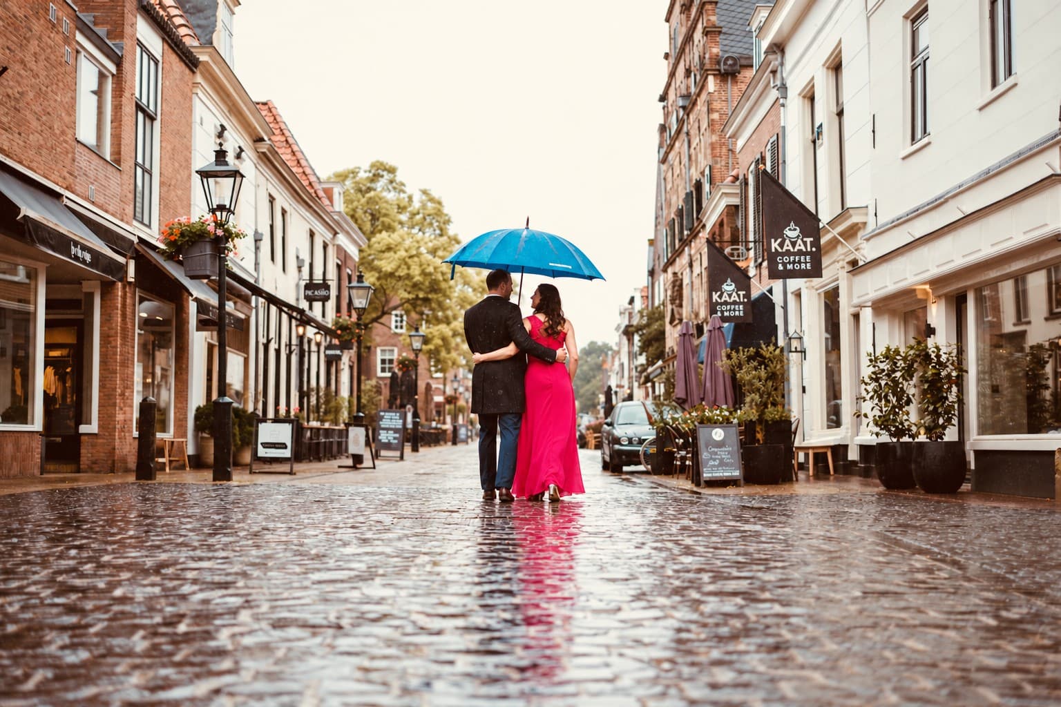 Stel arm in arm onder een blauwe paraplu in een regenachtige winkelstraat