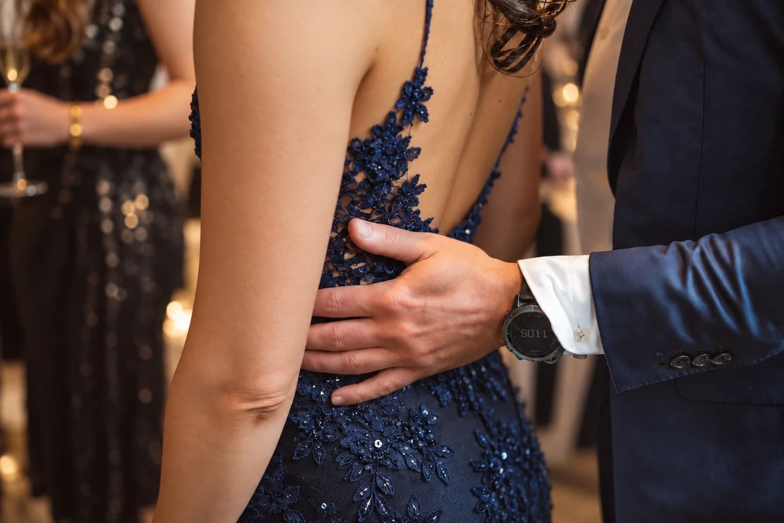 Hand van een man op de rug van een vrouw in een avondjurk, op een feest